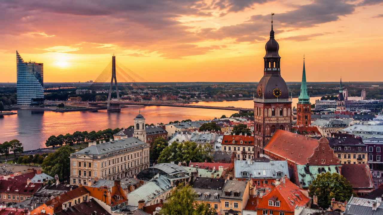 Riga’s Old Town skyline, church towers, and the Daugava River at sunset in Latvia.
