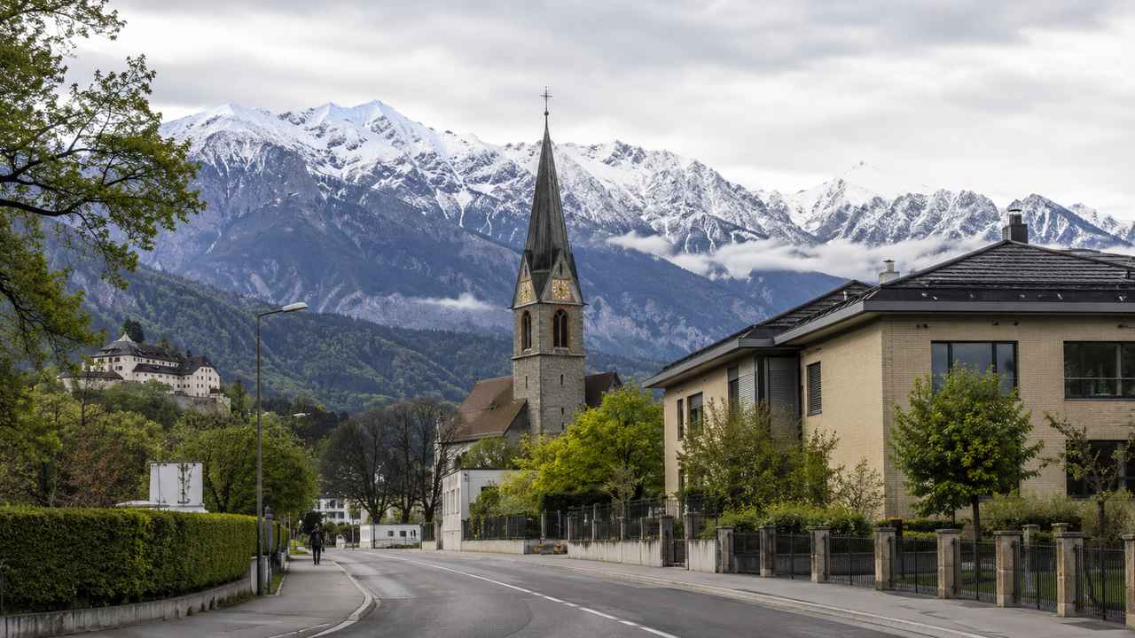 Quiet Alpine town scene in Liechtenstein with a church steeple, orderly street, ordinary buildings, and mountains in the background.